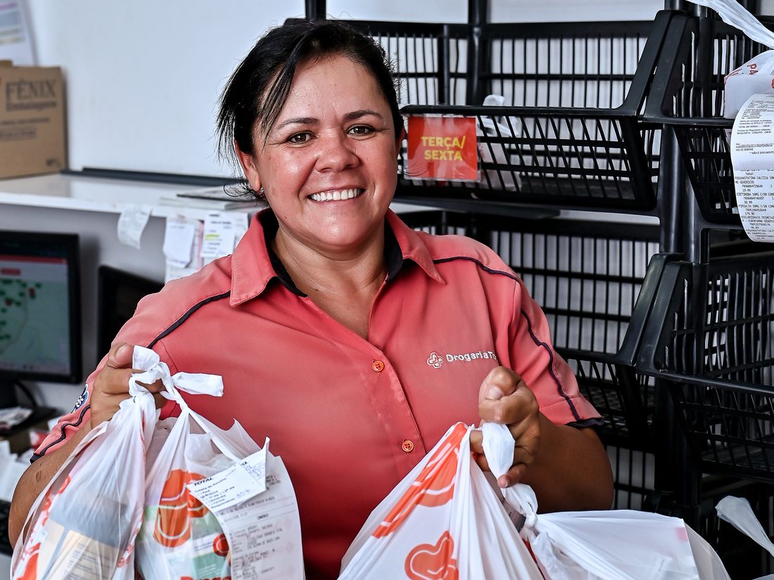 Colaboradora da drogaria segurando sacolas de entrega da Drogaria Total