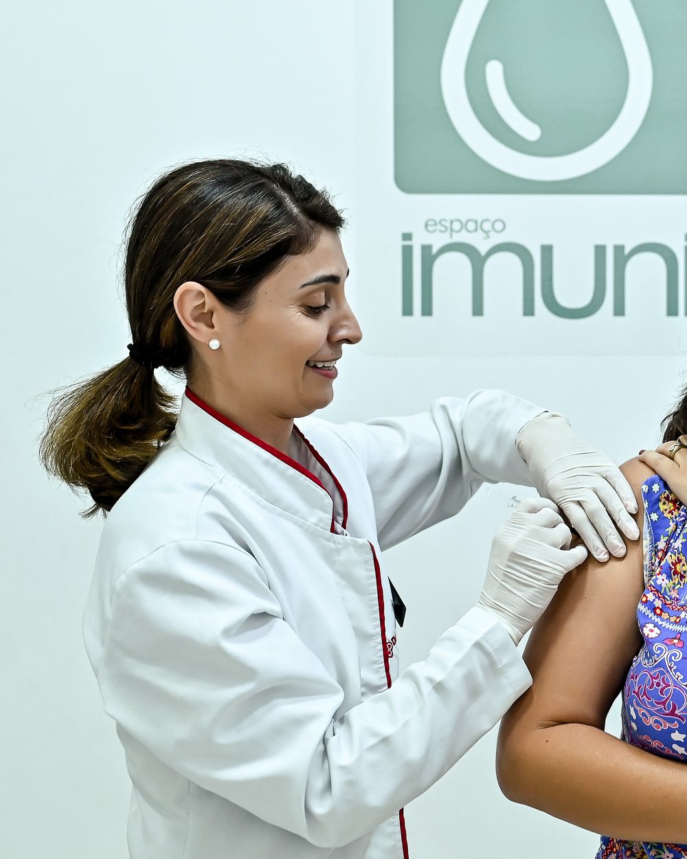 Farmacêutica aplicando uma vacina no braço de uma cliente, no Espaço Imuniza